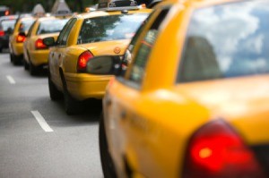 A row of taxi cabs driving on a city street.