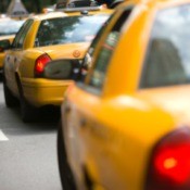 A row of taxi cabs driving on a city street.