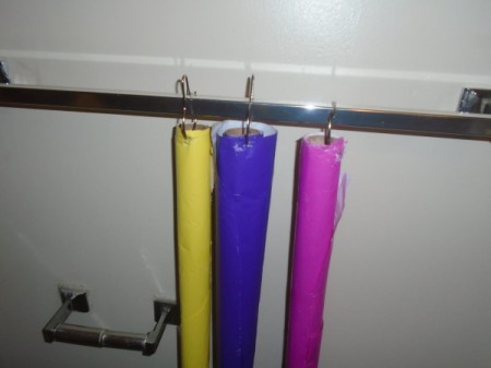Rolls of wrapping paper being hung by metal shower hooks.