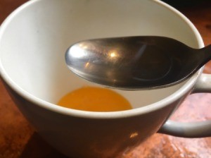 A teacup and a spoon with egg yolk in the bottom.