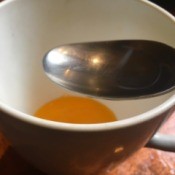A teacup and a spoon with egg yolk in the bottom.
