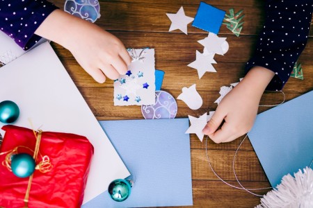 A girl making a homemade Christmas card with stickers and cutouts.