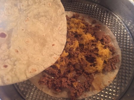 adding another tortilla to tortilla with ground beef mixture with cheese