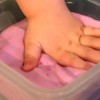 A child's hand in a container of pink flubber.