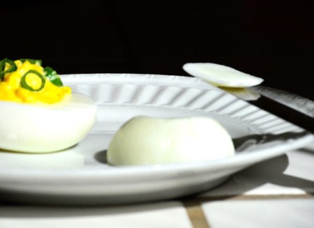 A plate with a deviled egg and a slice off of the bottom of another egg.