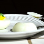A plate with a deviled egg and a slice off of the bottom of another egg.