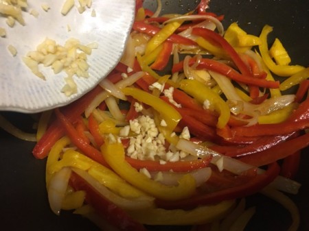 adding garlic to cooking onions, sliced red and yellow peppers