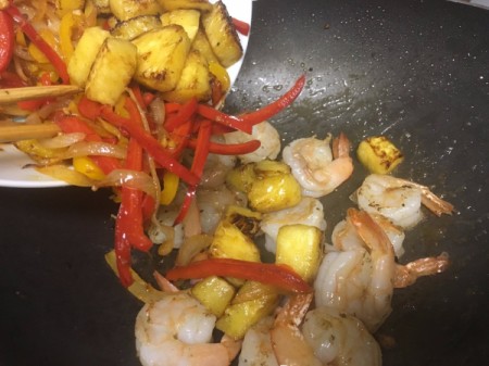 adding cooked peppers and pineapple to prawns