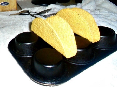 A muffin tin holding taco shells for filling.