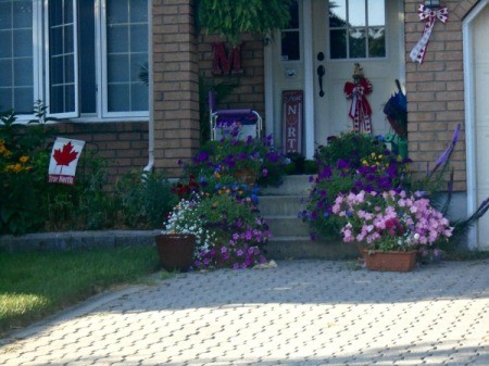 A front door with flowers on the staircase and yard.