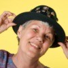 Woman with short grey hair adjusting a black hat.