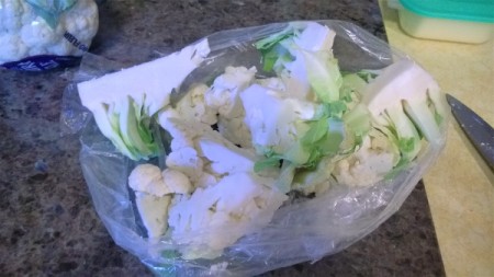 A bag that contains a head of cauliflower from the grocery store, cut in pieces