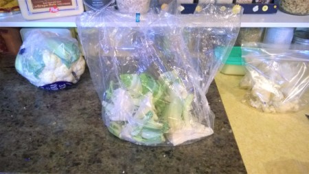A bag that contains a head of cauliflower from the grocery store, with the waste pieces left.