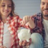 Father Helping Daughter Put Money in Piggy Bank