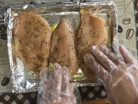 gloved hands seasoning chicken Breasts