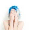 Woman with blue hair covering her face with her hands.