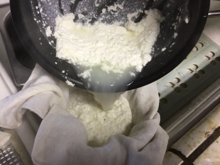 pouring curdled milk through cheesecloth