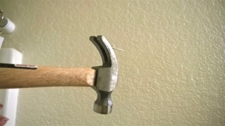 A hammer claw being used upside down to remove a nail from the wall.