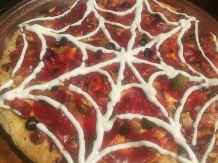 A spooky spider pizza, decorated with a ranch web.