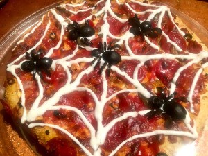 A spooky spider pizza, decorated with spider olives and a ranch web.