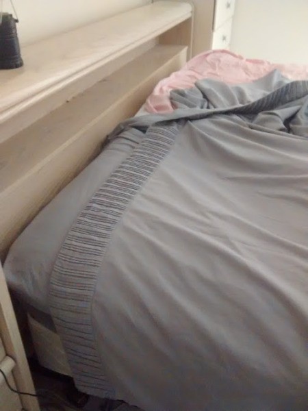 A bed in the process of having the sheets changed.