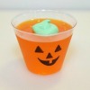 An orange cup of Jello with a Jack-o'-Lantern face.