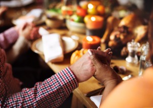 A group of people holding hands around a Thanksgiving dinner table.