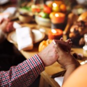 A group of people holding hands around a Thanksgiving dinner table.