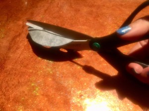 Scissors cutting through fine sandpaper to sharpen them.