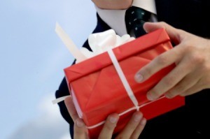 man holding gift in red box with white ribbon outdoors, close-up