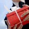 man holding gift in red box with white ribbon outdoors, close-up