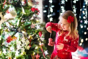 Child in red knitted Nordic reindeer sweater decorating Christmas tree