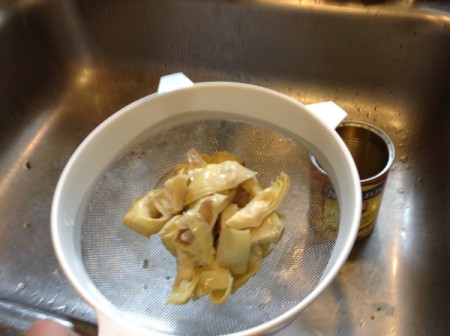 Canned artichoke hearts draining over a sink.