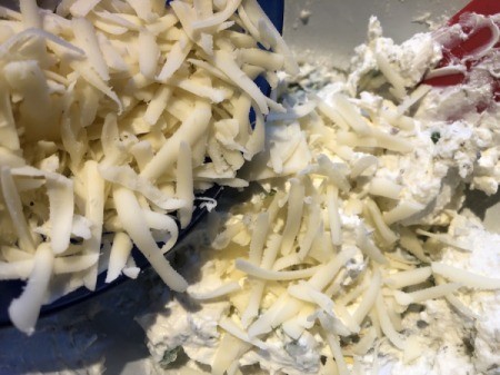 adding grated cheese to herbed cream cheese