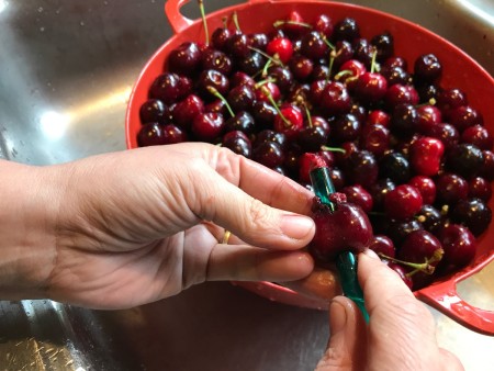 A straw being pushed through a whole cherry, to remove the pit.