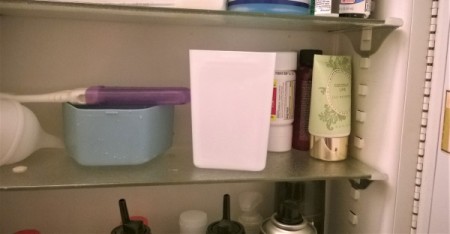 A white plastic container used as a cup in a medicine cabinet.