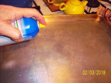 spraying oil on baking sheet