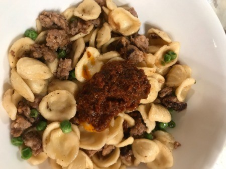 adding pesto sauce to pasta, peas, and sausage