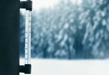 A thermometer with snowy weather outside.