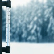 A thermometer with snowy weather outside.