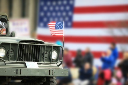 Close up of a Jeep with American flag flying on the hood and an American flag in the background.