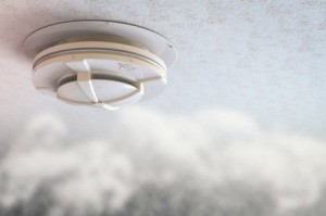 Smoke drifting up to a smoke alarm on the ceiling of a home.