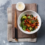 A bowl of stir fry chicken and vegetables with sesame seeds.