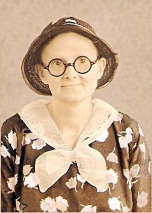 A sepia toned photo of an old fashioned woman with round glasses.