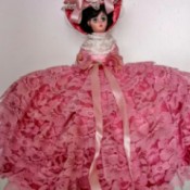 Identifying and Value of a Vintage Doll - small plastic doll wearing a ruffled dark pink dress and hat