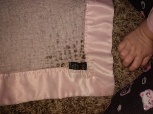 A pink cashmere baby blanket with satin trim, with some brown staining.