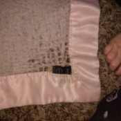 A pink cashmere baby blanket with satin trim, with some brown staining.