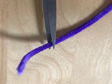 Scissors cutting a piece off a purple pipe cleaner.