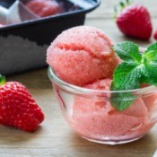 Homemade strawberry sorbet in a glass bowl with a sprig of mint.