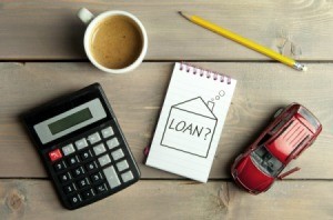 Calculator, cup of coffee, pencil, toy car and a notepad with "Loans?" written on it.